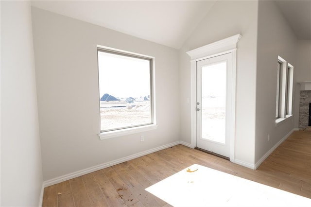 doorway featuring lofted ceiling, a stone fireplace, and light wood-type flooring