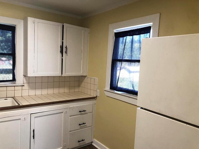 kitchen with decorative backsplash, white cabinetry, tile counters, and white refrigerator