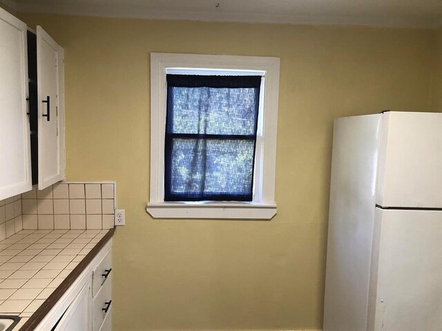 kitchen featuring white refrigerator, tile countertops, white cabinetry, and tasteful backsplash