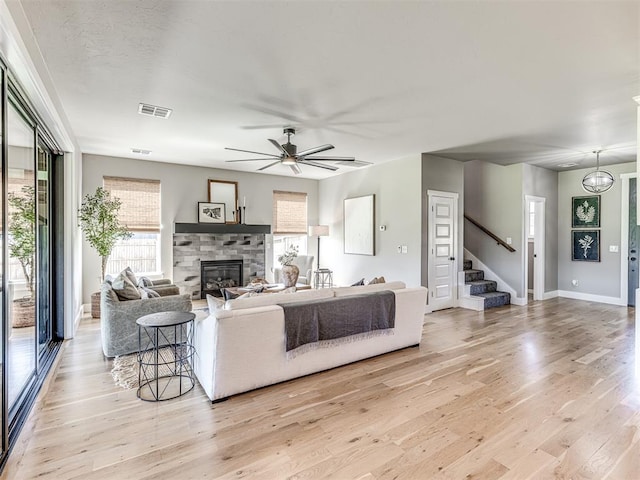 living room with a stone fireplace, ceiling fan, and light hardwood / wood-style floors