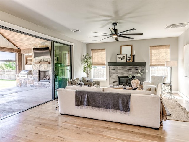 living room featuring light hardwood / wood-style floors, a stone fireplace, and ceiling fan