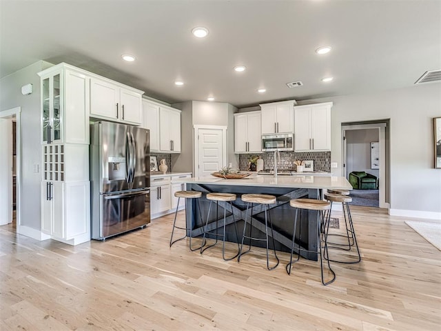 kitchen featuring white cabinets, light hardwood / wood-style flooring, an island with sink, and stainless steel appliances