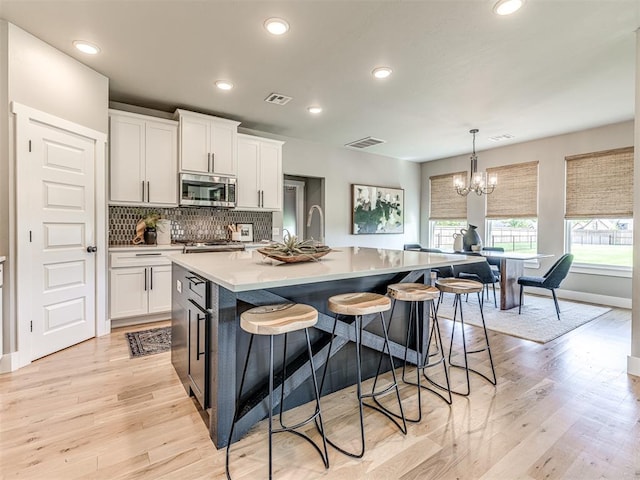 kitchen with white cabinets, an island with sink, stainless steel appliances, and light wood-type flooring