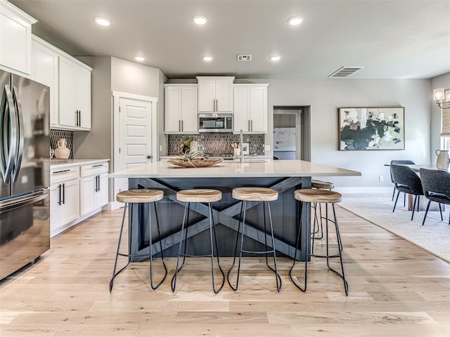 kitchen featuring stainless steel appliances, white cabinetry, a center island with sink, and sink