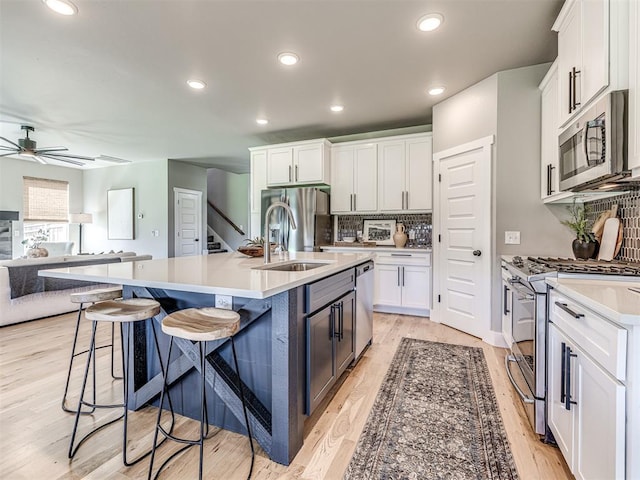 kitchen with an island with sink, sink, white cabinets, and stainless steel appliances