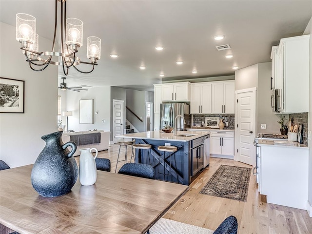 kitchen featuring sink, light wood-type flooring, an island with sink, appliances with stainless steel finishes, and white cabinetry