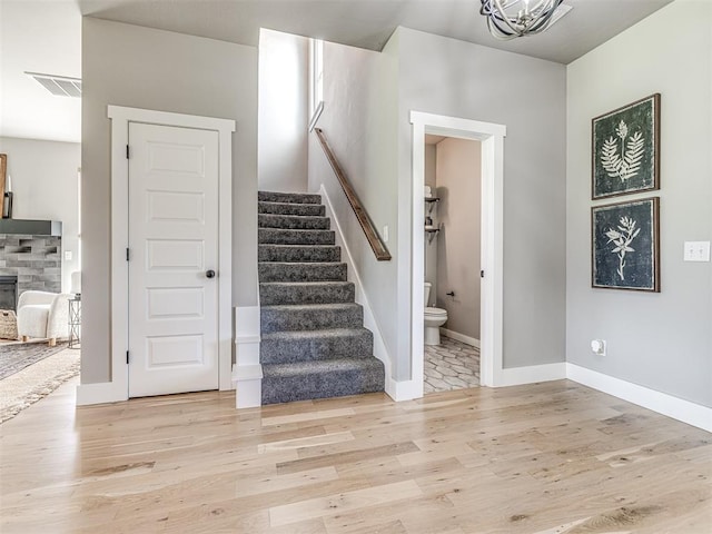 stairway with a chandelier, hardwood / wood-style floors, and a stone fireplace