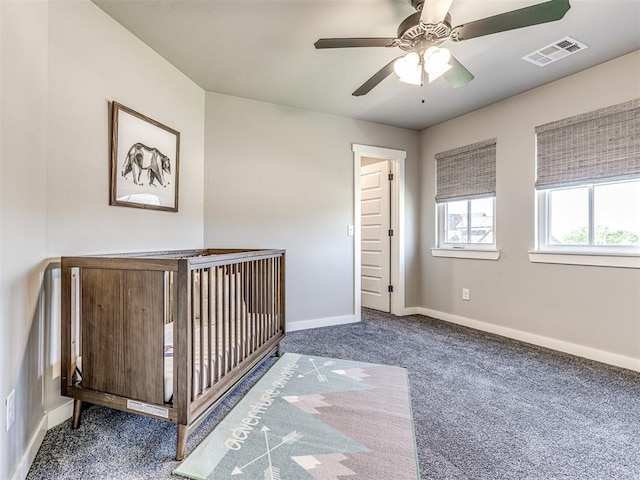 unfurnished bedroom with dark colored carpet, ceiling fan, and a nursery area