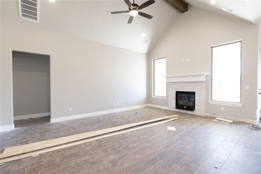 unfurnished living room with a fireplace, high vaulted ceiling, light wood-type flooring, ceiling fan, and beam ceiling