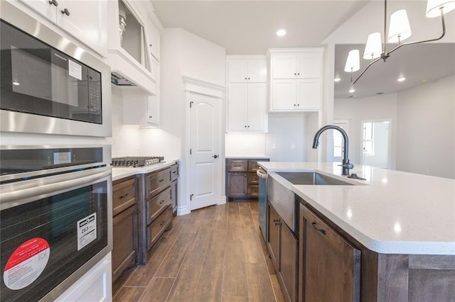 kitchen with a center island with sink, white cabinets, dark wood-style floors, stainless steel appliances, and pendant lighting