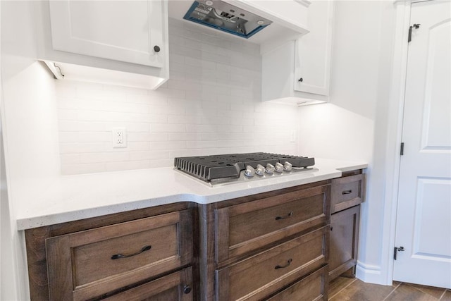 kitchen featuring stainless steel gas stovetop, backsplash, white cabinetry, ventilation hood, and light stone countertops