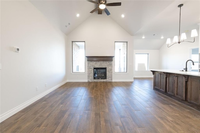 unfurnished living room featuring a stone fireplace, a sink, visible vents, a ceiling fan, and dark wood finished floors