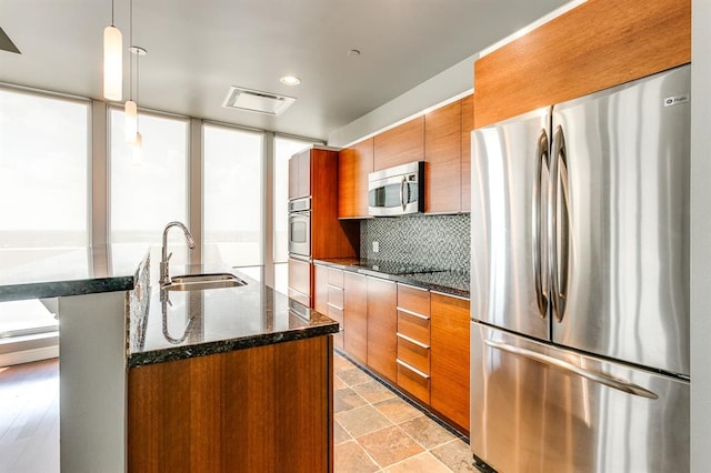 kitchen featuring decorative light fixtures, sink, dark stone countertops, a kitchen island with sink, and stainless steel appliances