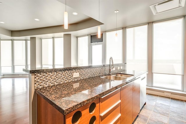 kitchen with decorative light fixtures, sink, dark stone countertops, decorative backsplash, and a kitchen island with sink