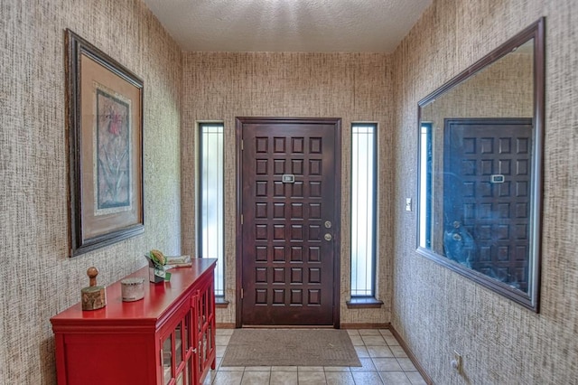 foyer entrance with light tile patterned flooring, a textured ceiling, and baseboards