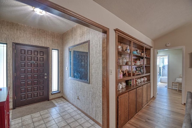 foyer with lofted ceiling, a textured ceiling, baseboards, and wallpapered walls