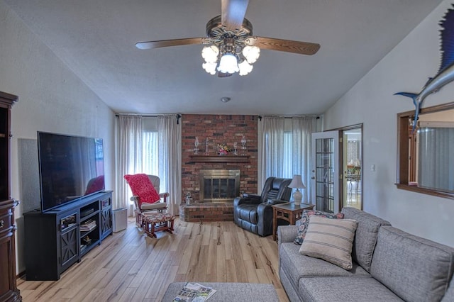 living area with lofted ceiling, light wood-type flooring, a fireplace, and ceiling fan