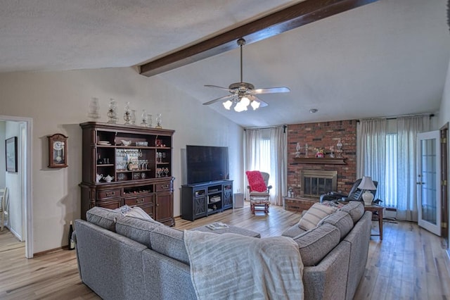 living room with a ceiling fan, a fireplace, vaulted ceiling with beams, and light wood finished floors