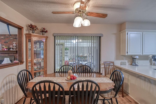 dining area with a textured ceiling, light wood-type flooring, and a ceiling fan