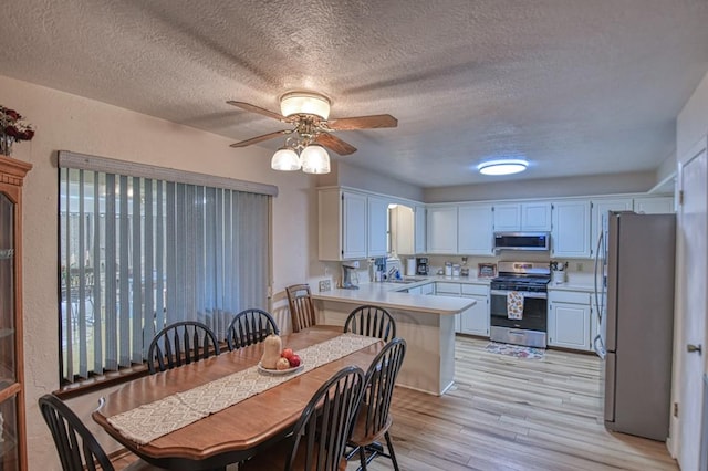 kitchen featuring white cabinets, appliances with stainless steel finishes, a peninsula, light countertops, and light wood-style floors