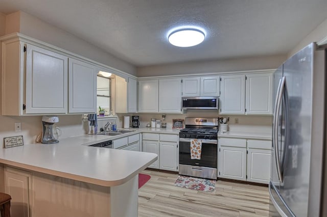 kitchen featuring white cabinets, appliances with stainless steel finishes, a peninsula, light countertops, and a sink