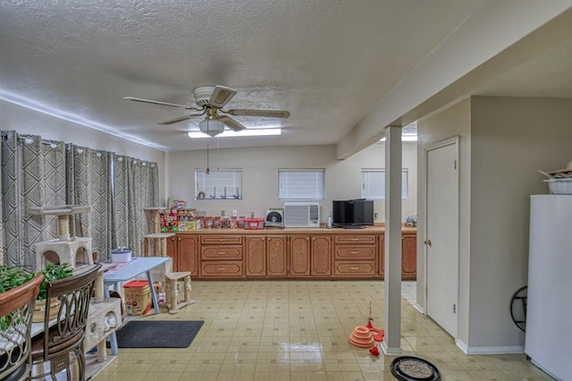 kitchen with a textured ceiling, light floors, brown cabinetry, and a ceiling fan