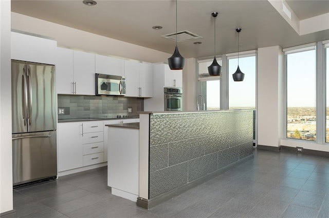 kitchen with appliances with stainless steel finishes, plenty of natural light, pendant lighting, and white cabinets