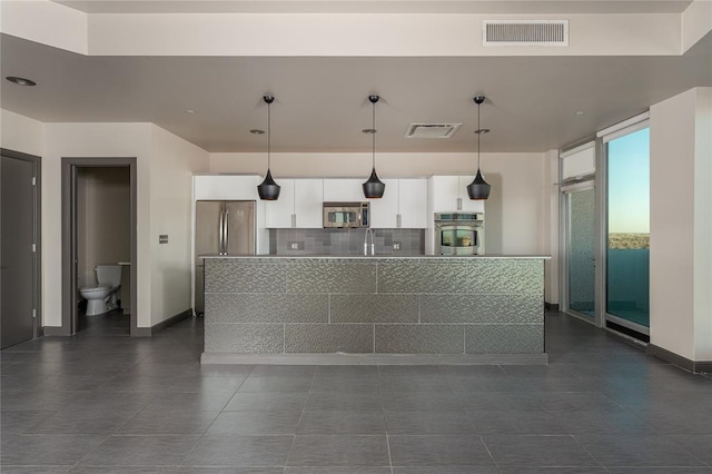 kitchen featuring hanging light fixtures, stainless steel appliances, an island with sink, white cabinets, and decorative backsplash