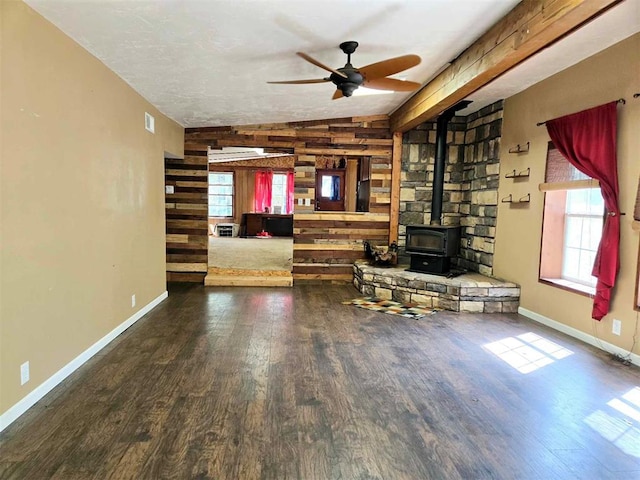 unfurnished living room featuring dark hardwood / wood-style flooring, a wood stove, ceiling fan, and wood walls