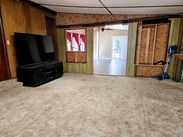 carpeted living room with ceiling fan and wood walls