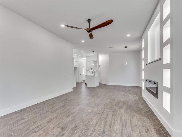 unfurnished living room featuring light wood-type flooring, heating unit, ceiling fan, and sink