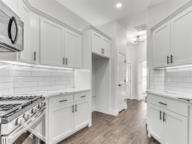 kitchen with tasteful backsplash, light stone counters, dark hardwood / wood-style floors, white cabinets, and appliances with stainless steel finishes