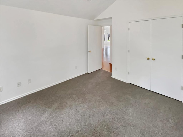 unfurnished bedroom with a closet, dark carpet, and vaulted ceiling