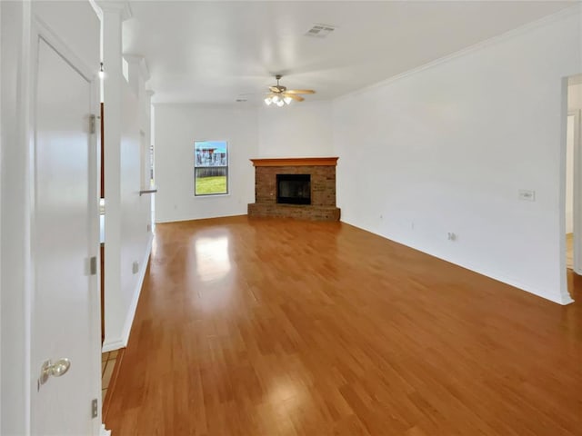 unfurnished living room featuring ceiling fan, wood-type flooring, ornamental molding, and a brick fireplace