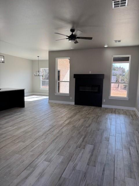 unfurnished living room with ceiling fan with notable chandelier and wood-type flooring