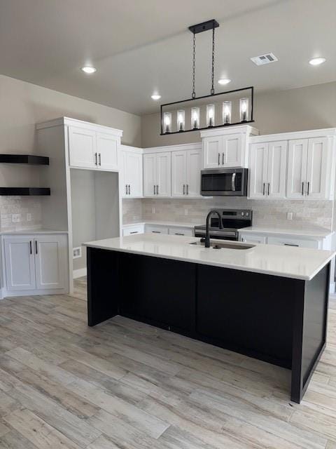 kitchen featuring decorative light fixtures, white cabinets, sink, and an island with sink