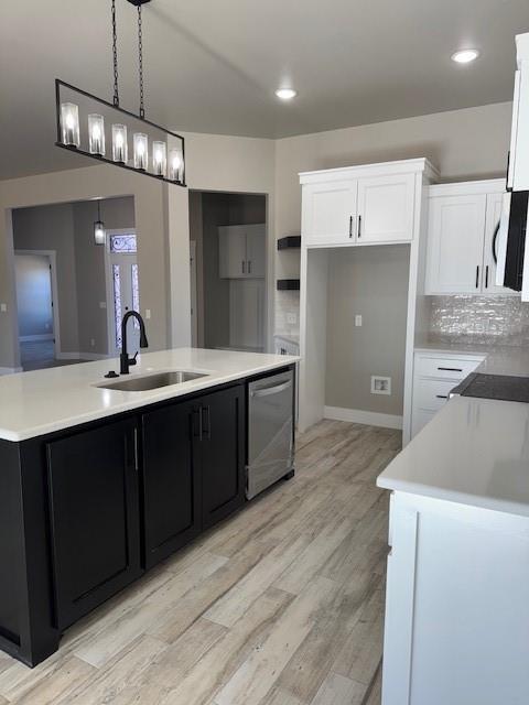 kitchen featuring pendant lighting, sink, white cabinetry, and an island with sink