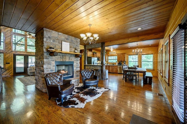 living room with wooden ceiling, a stone fireplace, a notable chandelier, hardwood / wood-style floors, and wooden walls