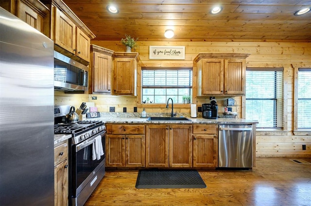 kitchen with light stone counters, sink, stainless steel appliances, and wooden walls