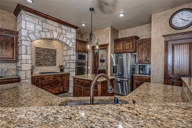 kitchen featuring dark brown cabinetry, sink, stainless steel appliances, light stone counters, and pendant lighting