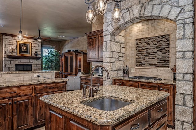 kitchen with ceiling fan, stainless steel gas cooktop, a kitchen island with sink, sink, and decorative light fixtures