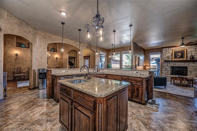 kitchen with a stone fireplace, sink, decorative light fixtures, ceiling fan, and a large island