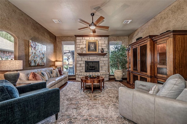 living room with a textured ceiling, ceiling fan, and a fireplace