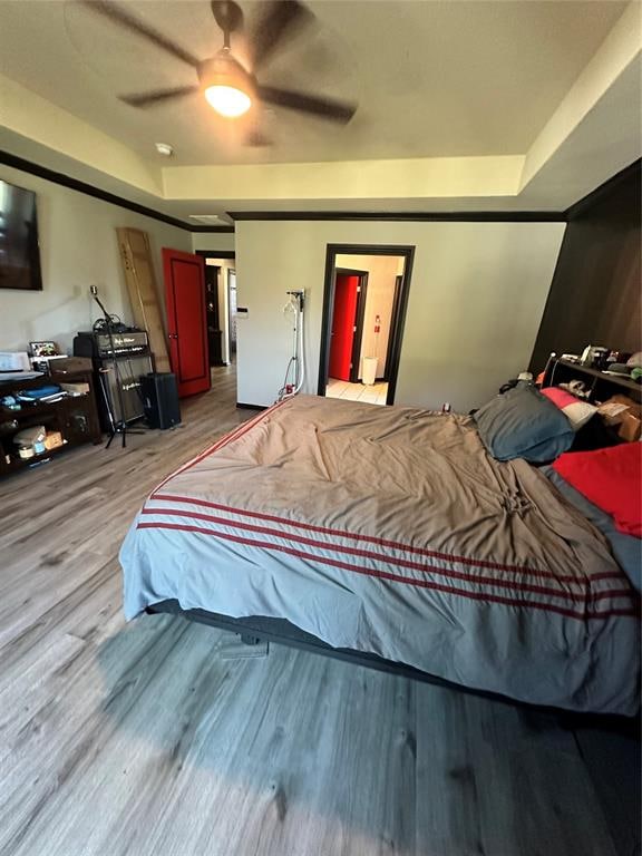 bedroom featuring a tray ceiling, ceiling fan, and light wood-type flooring