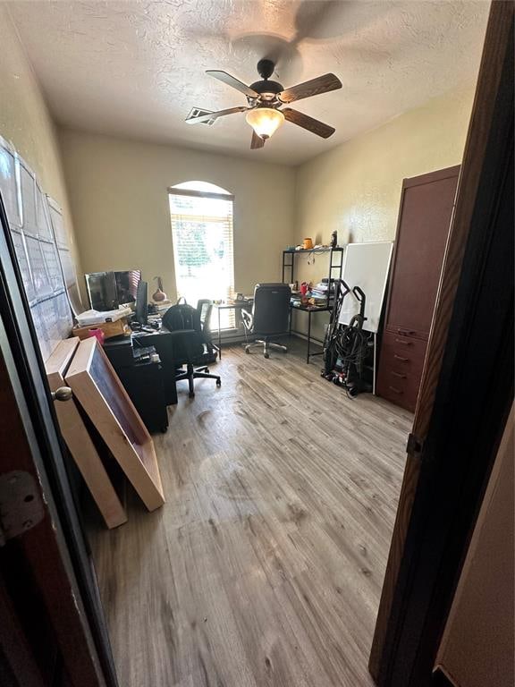 home office with ceiling fan, light hardwood / wood-style floors, and a textured ceiling