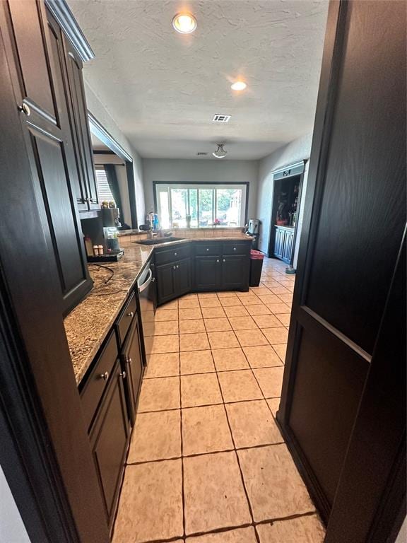 kitchen featuring stainless steel dishwasher, a textured ceiling, sink, stone counters, and light tile patterned flooring