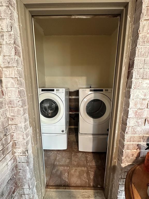 laundry area featuring tile patterned floors, separate washer and dryer, and brick wall