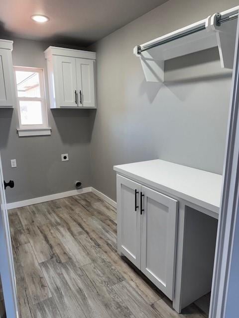 washroom featuring electric dryer hookup, light hardwood / wood-style flooring, and cabinets