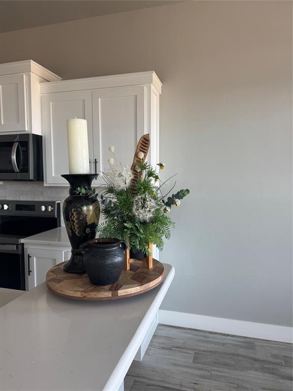 kitchen with electric range oven, wood finished floors, baseboards, white cabinets, and stainless steel microwave