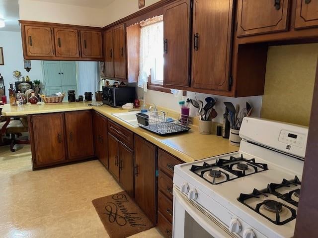 kitchen featuring white range with gas stovetop, kitchen peninsula, and sink